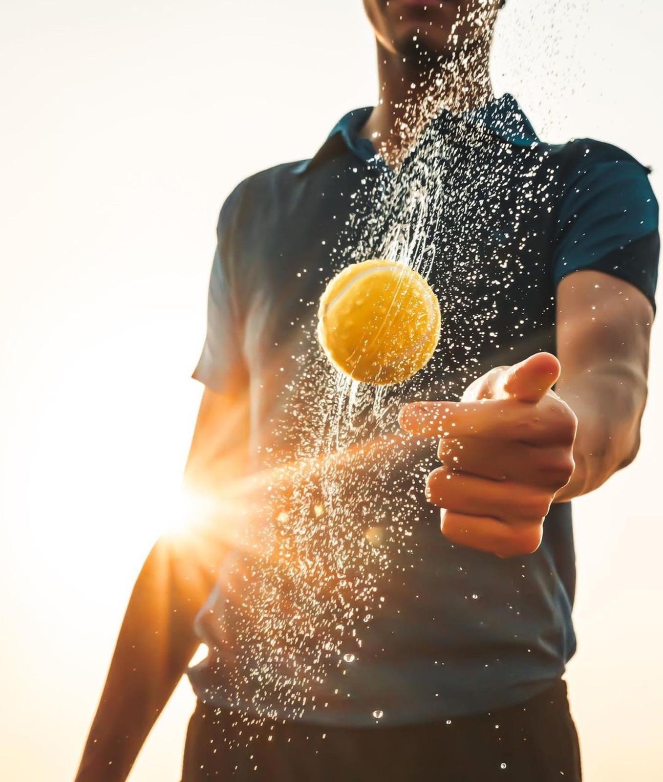 A player pointing forward as a tennis ball sprays water